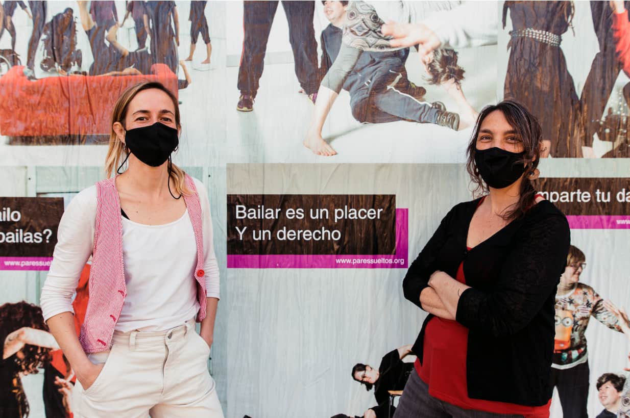 Leticia y violeta posando en una pared con carteles